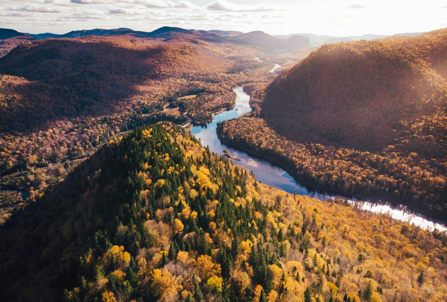 A breathtaking aerial view of fall foliage in Québec's National Park, highlighting vibrant autumn colors and serene river scenery.